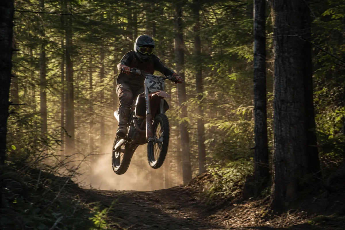 Dirt bike rider mid-jump on a forest trail